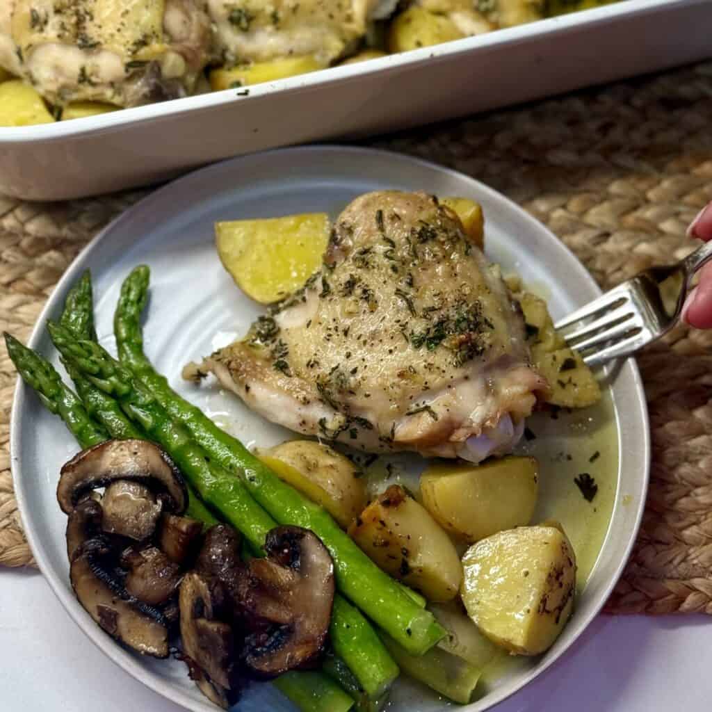 A plate of roasted chicken thighs and potatoes with asparagus.