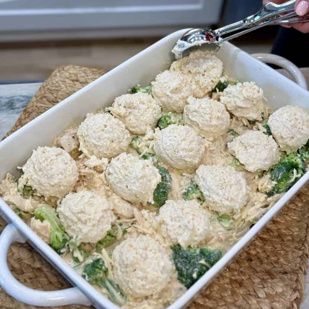 Scooping biscuits on top of a chicken casserole.