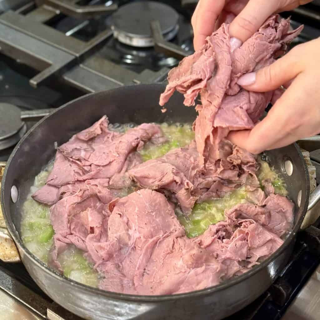 Adding shaved beef to a pan of onion and green pepper.