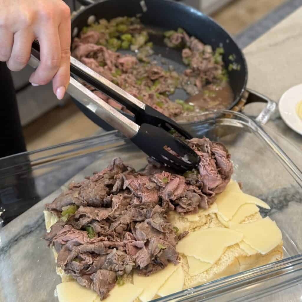 Adding cooked deli shaved beef and vegetables to slider buns.