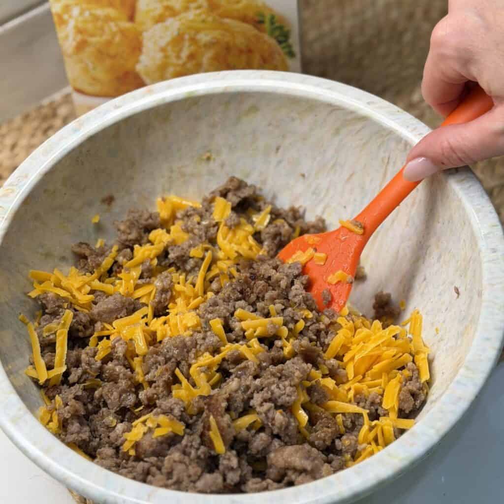 Mixing sausage biscuit muffin batter in a bowl.