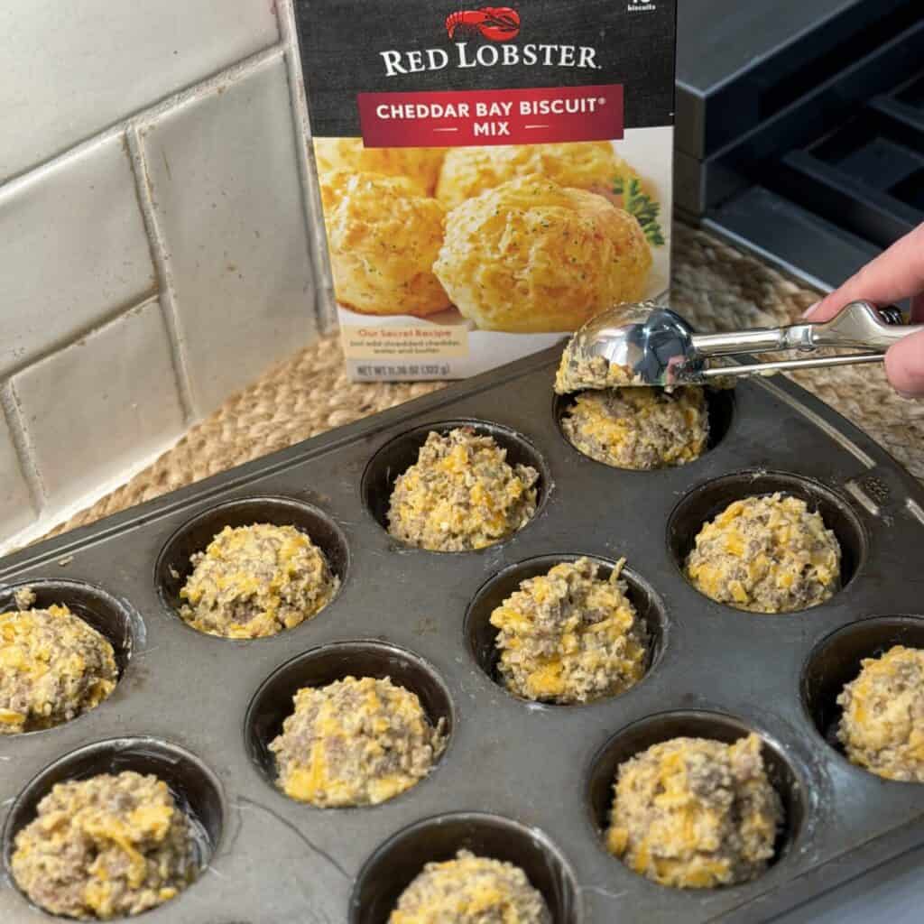 Scooping sausage biscuit muffins in a pan.