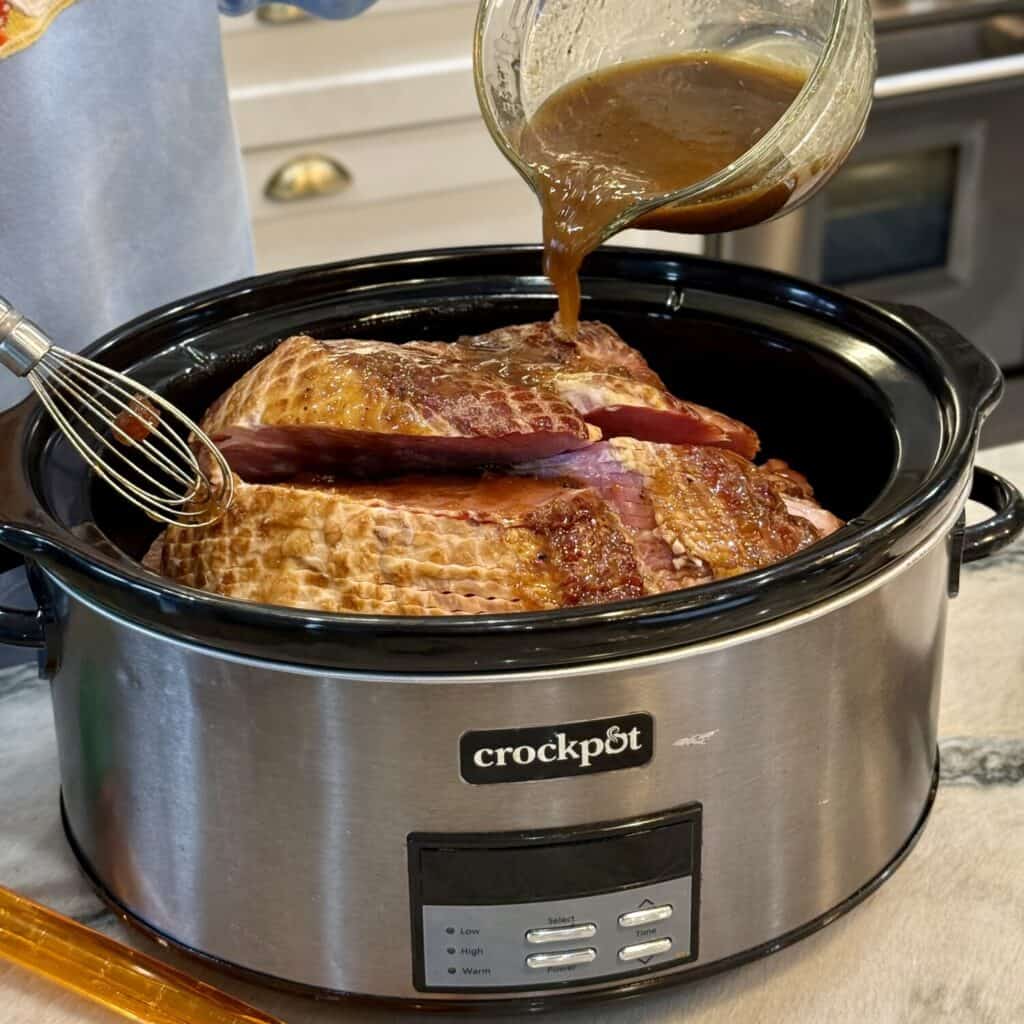 Pouring glaze on top of ham in a crockpot.
