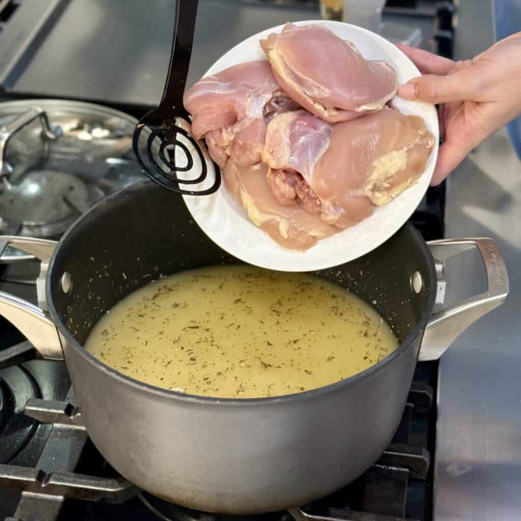 Adding chicken to a pan of broth.