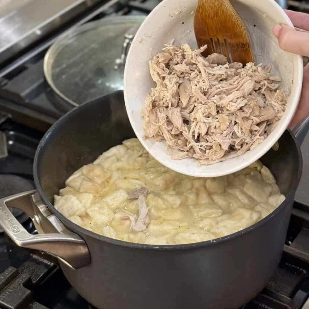 Adding chicken to a pan of Chicken and Dumplings with Canned Biscuits.