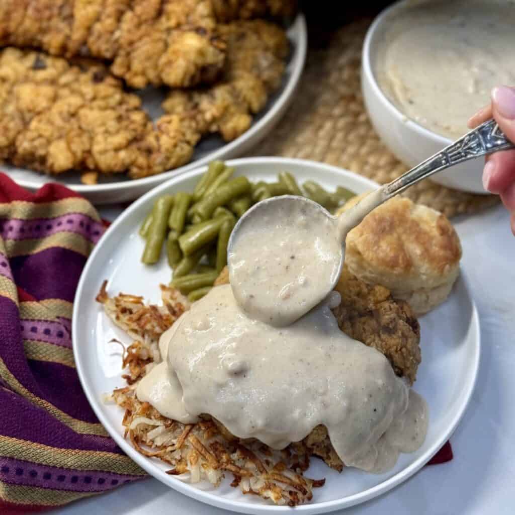 A plate of chicken fried steak, gravy, biscuit and green beans.