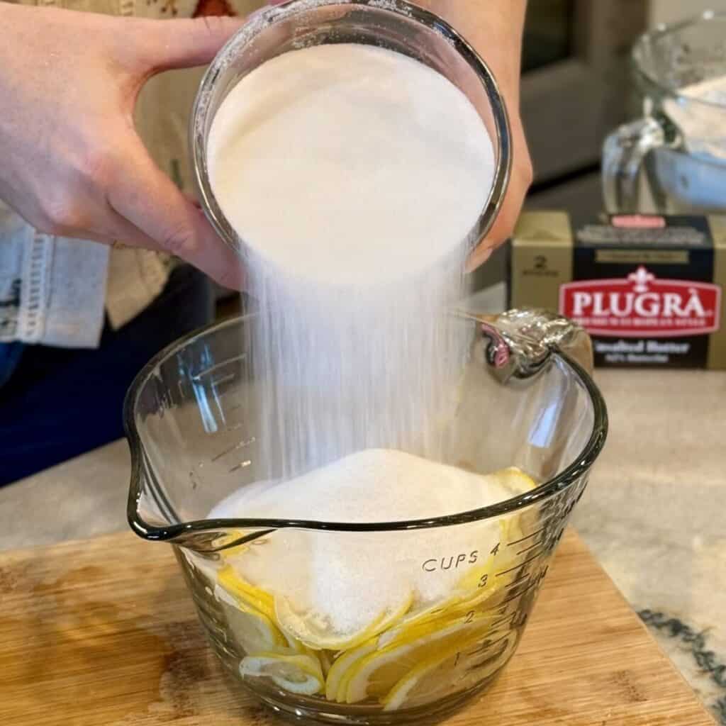 Adding sugar to lemons in a bowl.