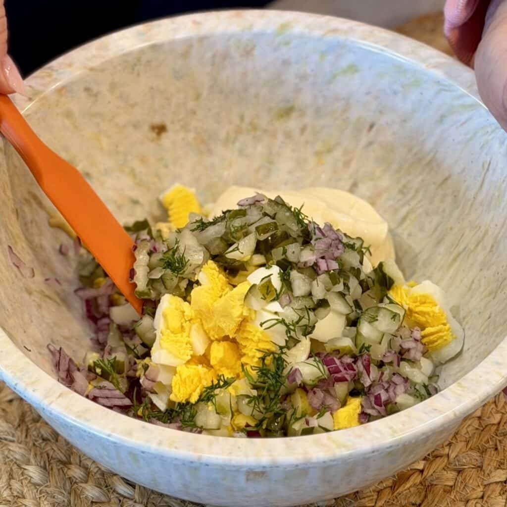 Mixing the ingredients for dill pickle egg salad.