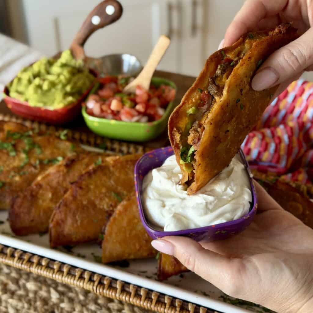 Dipping sheet pan tacos into sour cream.