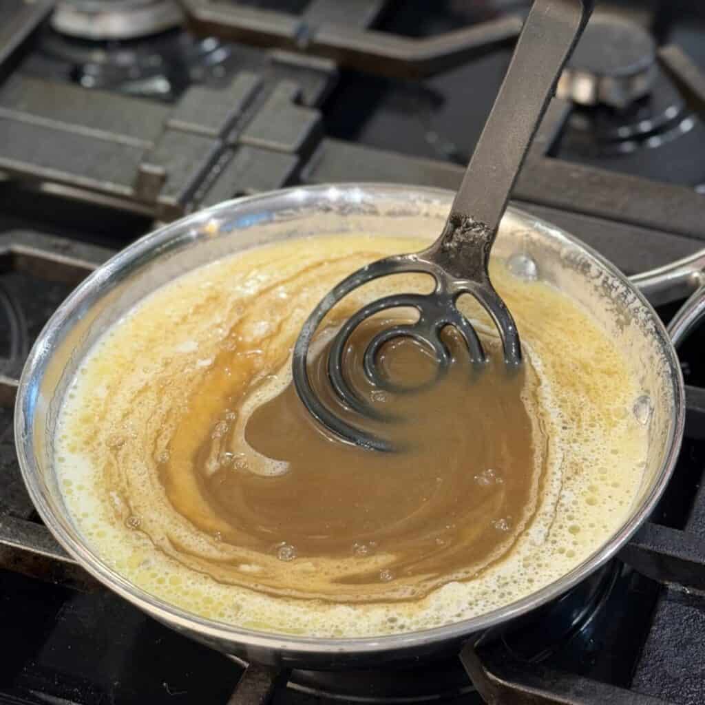 Whisking together the ingredients of brown sugar butter sauce in a pan.