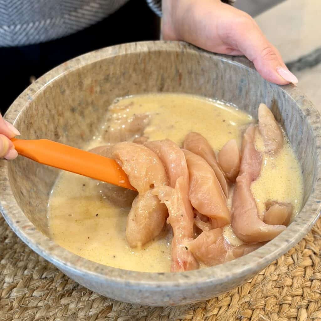 Adding chicken in the marinate bowl.