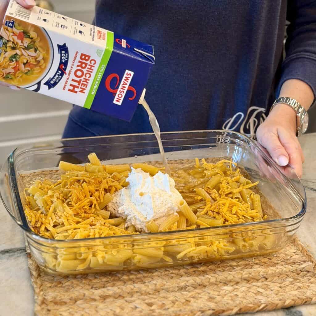 Adding chicken broth to the dish of pasta.