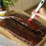 Adding barbecue sauce to rack of ribs.