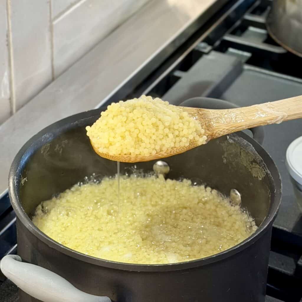 Cooked pasta on a spoon over a pan.