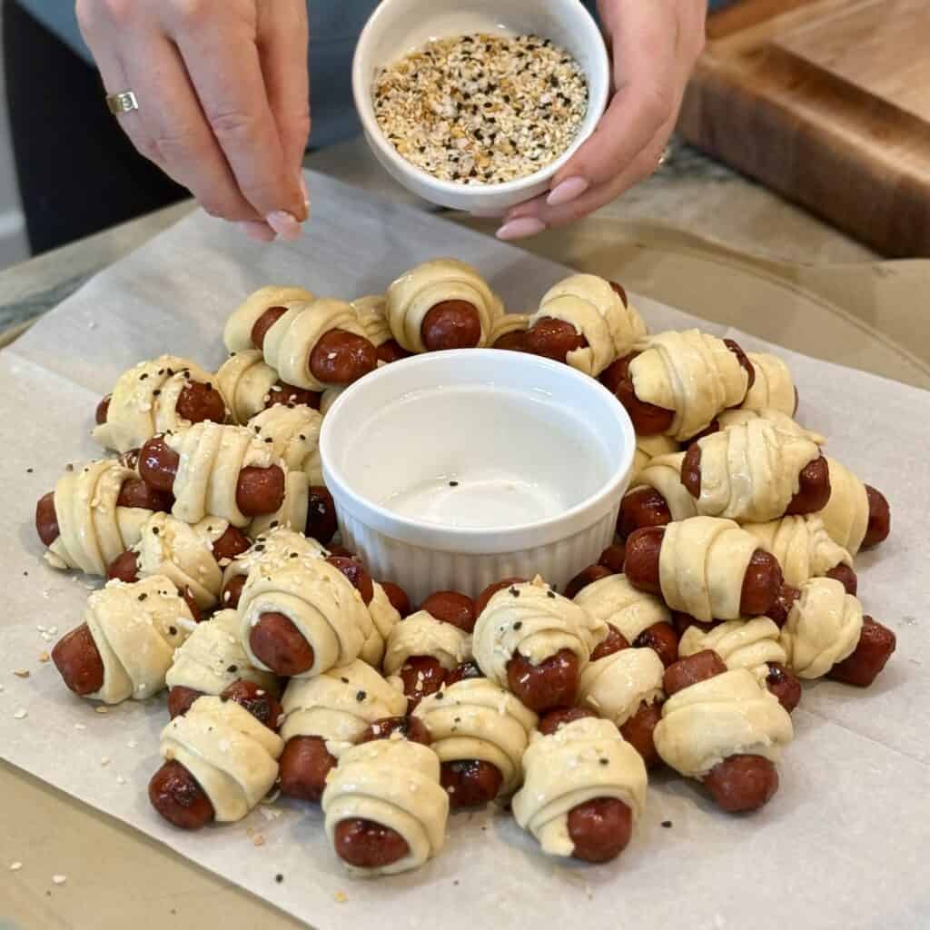 Adding seasoning to the pigs in a blanket.