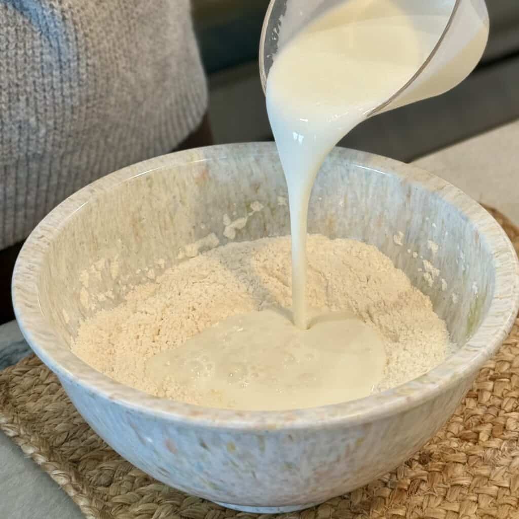 Adding cream to the bowl of flour.