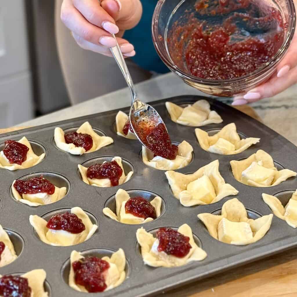 Adding jam to brie bites.