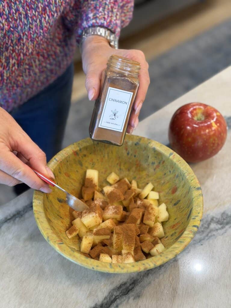 Adding cinnamon to the bowl of apples.